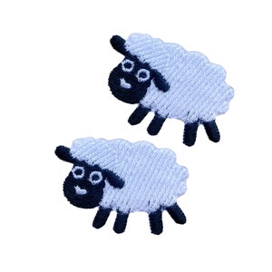 May include: Two white sheep with black faces and legs. The sheep are embroidered and have a fluffy texture.