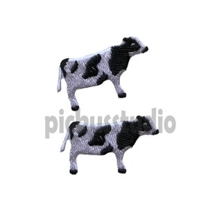 以下が含まれることがあります： 黒と白の刺繍された牛のパッチが2つ。牛は右を向いており、白い背景に黒い斑点があります。