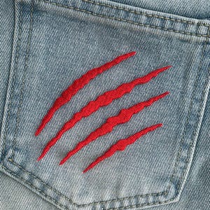 Puede incluir: Primer plano de un bolsillo de mezclilla azul con un diseño de garra bordada en rojo.
