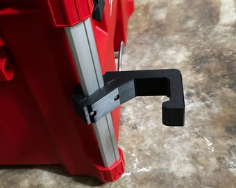 May include: A black plastic hook attached to a red and silver toolbox. The hook is designed to hold items such as a rope or a tool.