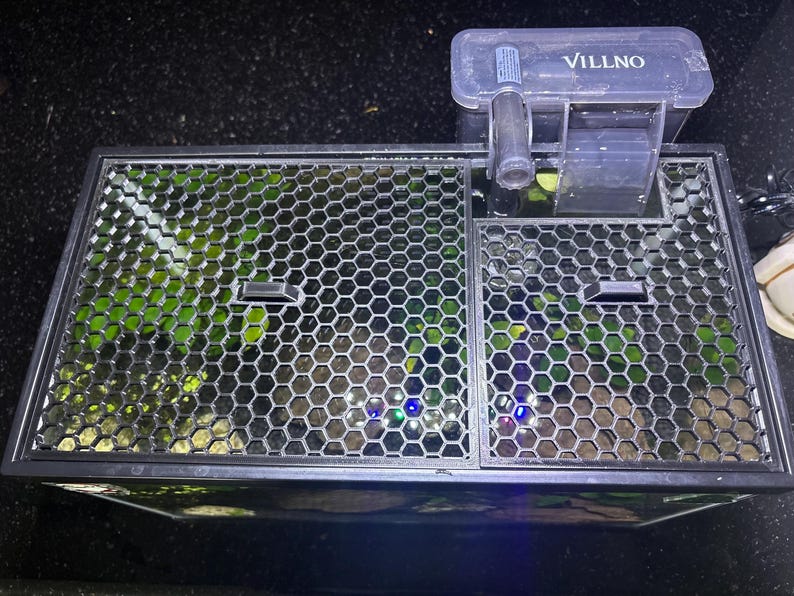 Top-down view of a fish tank with a black 3D-printed honeycomb mesh aquarium lid cover installed. The mesh design allows for optimal light penetration and airflow while preventing fish from jumping. The lid features two built-in feeding ports and is fitted around a hang-on-back filter. A functional and aesthetic solution for aquarium protection, ideal for planted tanks and open-top aquariums.