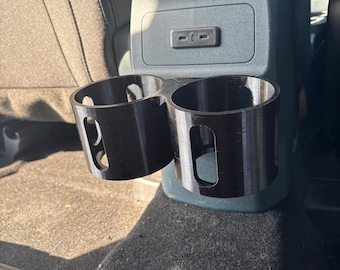May include: Black plastic car cup holder with two slots for drinks. The holder is attached to the back of a car seat.