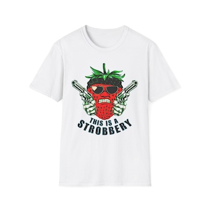 May include: White t-shirt with a cartoon strawberry wearing sunglasses and a black hat, holding two guns. The text "THIS IS A STROBBERY" is printed below the strawberry in a stylized font.