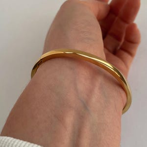 Peut inclure: Un bracelet jonc en or avec une finition simple et polie. Le bracelet est ouvert et poss&egrave;de un fermoir &agrave; charni&egrave;re.