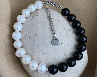 May include: A black and white beaded bracelet with a stainless steel clasp. The bracelet has white pearls on one side and black beads on the other. The clasp has a small tag that says "S.Steel".