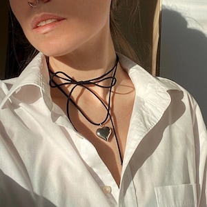 May include: A black choker necklace with a silver heart pendant. The necklace is layered and has a bow at the front.