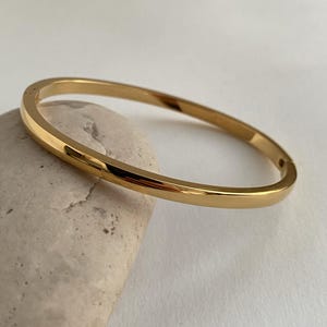 Peut inclure: Un bracelet jonc simple en or. Le bracelet est fait d'un m&eacute;tal lisse et brillant et a une finition polie.