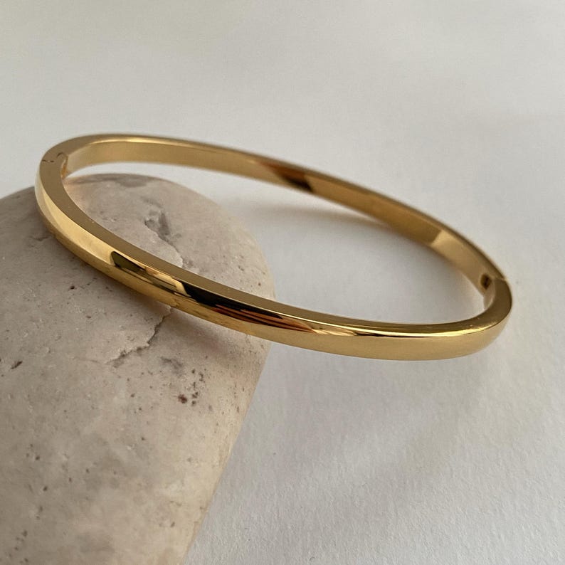 Peut inclure: Un bracelet jonc simple en or. Le bracelet est fait d'un m&eacute;tal lisse et brillant et a une finition polie.