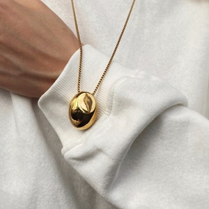 Puede incluir: Un collar de cadena dorada con un gran colgante ovalado liso.