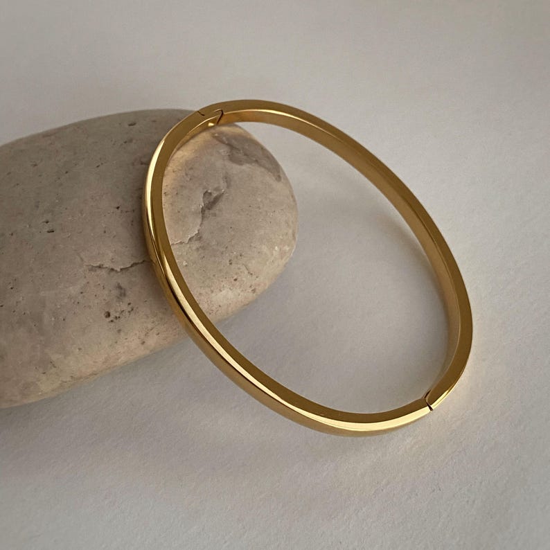 Peut inclure: Un bracelet jonc dor&eacute; &agrave; l'aspect simple et arrondi. Le bracelet est en m&eacute;tal et a une finition lisse.