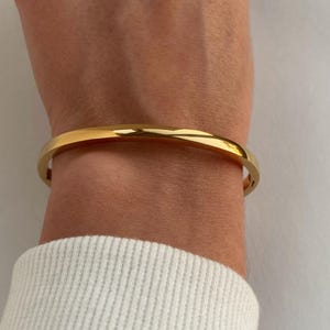 Peut inclure: Un bracelet jonc en or port&eacute; au poignet. Le bracelet est simple et a une finition lisse et polie.
