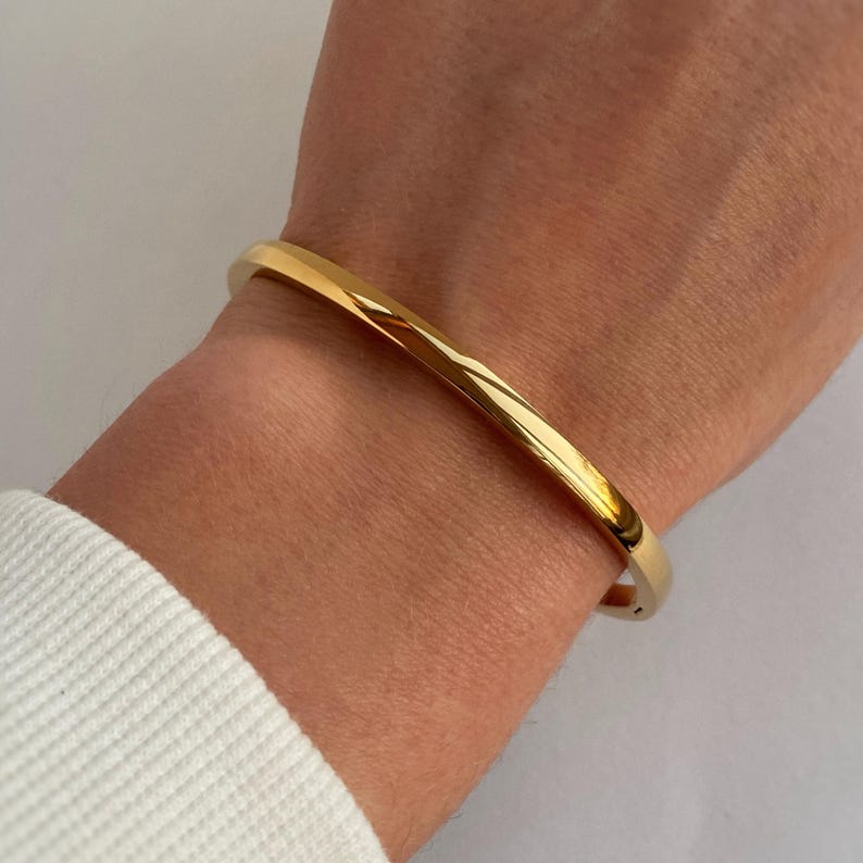 Peut inclure: Un bracelet jonc en or port&eacute; au poignet. Le bracelet est simple et &eacute;l&eacute;gant, avec une finition lisse et polie.