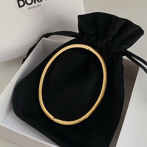 Peut inclure: Un bracelet jonc en or dans une pochette en velours noir. La pochette a une fermeture &agrave; cordon et est plac&eacute;e dans une bo&icirc;te blanche avec le mot "DORAJ JEWELRY" imprim&eacute; sur le couvercle.