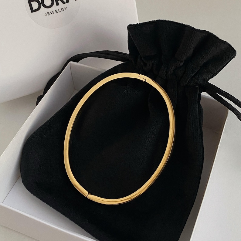 Peut inclure: Un bracelet jonc en or dans une pochette en velours noir. La pochette a une fermeture &agrave; cordon et est plac&eacute;e dans une bo&icirc;te blanche avec le mot "DORAJ JEWELRY" imprim&eacute; sur le couvercle.
