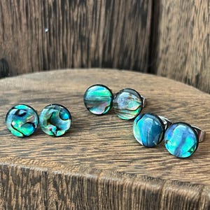 May include: Four pairs of iridescent abalone shell earrings. The earrings are round and have a silver backing. The shells are a mix of green, blue, and black.