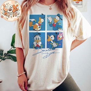 May include: A white t-shirt with a blue and yellow cartoon image of Donald Duck in four different expressions. The text "Donald Duck" is written in black cursive below the image.