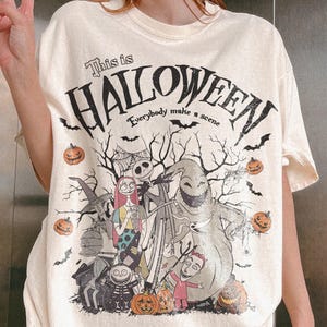 Pu&ograve; includere: T-shirt color crema con grafica da "Nightmare Before Christmas". Il design include Jack Skellington, Sally, Oogie Boogie e altri personaggi, con la scritta "This is Halloween" e "Everybody make a scene."