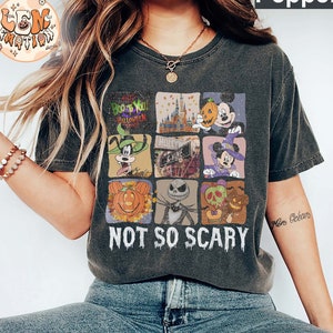 May include: A dark gray t-shirt with a vintage-style graphic featuring various Disney characters and Halloween imagery. The graphic includes Mickey Mouse, Goofy, Jack Skellington, and a pumpkin. The text "Boo to You Halloween" and "Not So Scary" are also included in the graphic.