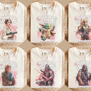 K&ouml;nnte beinhalten: Cremefarbene T-Shirts mit Star Wars-Charakteren und dem Text "STAR WARS ATTACK OF THE CLONES". Die Shirts zeigen Bilder von Prinzessin Leia, Yoda, Boba Fett, Anakin Skywalker, Darth Vader und Chewbacca.