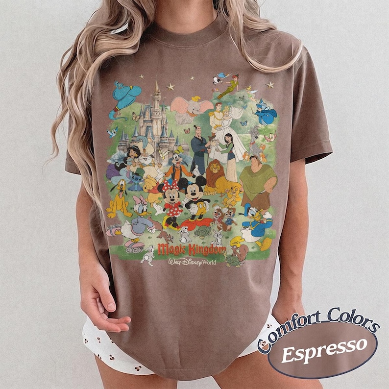 May include: A brown short-sleeve t-shirt featuring a large graphic print of various Disney characters, including Mickey Mouse, Minnie Mouse, and Cinderella, in front of a castle. The text reads Magic Kingdom Walt Disney World in red and white.