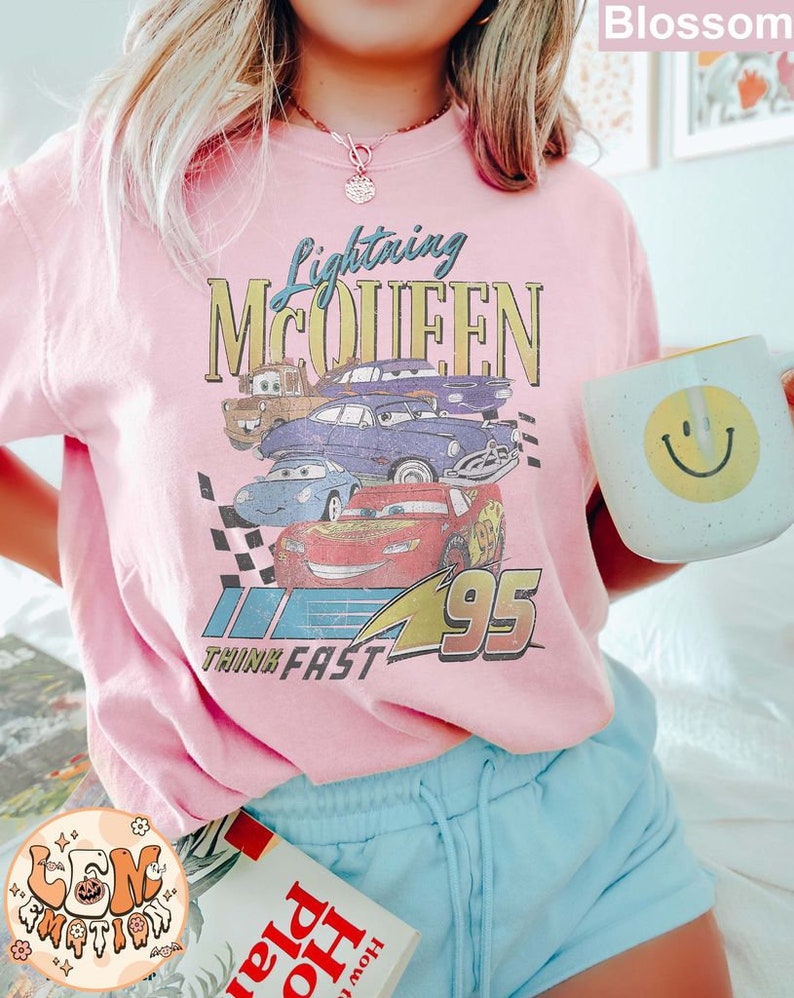 May include: Pink t-shirt with a graphic of Lightning McQueen from the Cars movie. The graphic includes the text "Lightning McQueen" and "Think Fast 95".