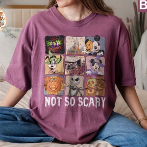 May include: A purple t-shirt with a graphic print of various Disney characters celebrating Halloween. The text "Boo to You! Halloween Time" and "Not So Scary" are printed on the shirt.