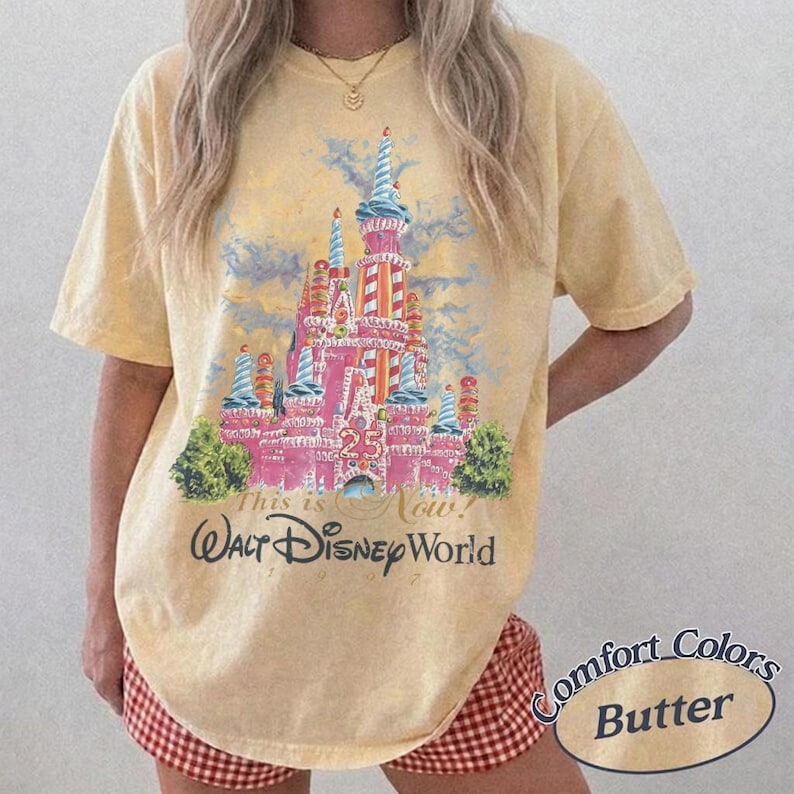 May include: Butter-colored t-shirt featuring a pink and red castle graphic with blue turrets and the text "This is Now! Walt Disney World." The shirt has short sleeves and a relaxed fit. The words "Comfort Colors Butter" are printed on the bottom right.
