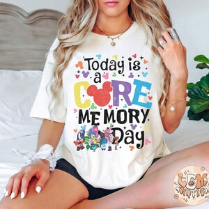 以下が含まれることがあります： 「Today is a CORE MEMORY Day」というカラフルなグラフィックがプリントされた白いTシャツ。ミッキーマウスの頭と映画「インサイド・ヘッド」のキャラクターが描かれています。