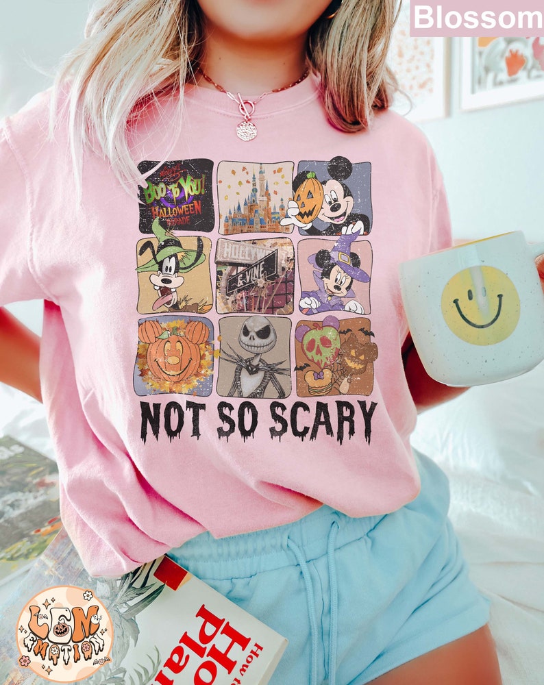 May include: Pink t-shirt with a graphic of a collage of various Disney characters celebrating Halloween. The characters include Mickey Mouse, Goofy, and Jack Skellington. The text "Boo to You! Halloween Parade" and "Not So Scary" are printed on the shirt.