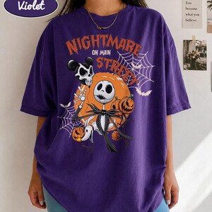 Pu&ograve; includere: Una t-shirt viola a maniche corte con una stampa grafica che riporta il testo Nightmare on Main Street, un personaggio scheletro, un cane fantasma, zucche, ragnatele e pipistrelli. La maglia presenta un girocollo e una vestibilit&agrave; ampia.
