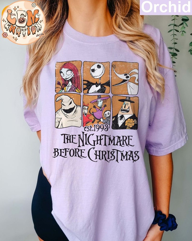 May include: A purple t-shirt with a graphic print of characters from the movie "The Nightmare Before Christmas". The text "est. 1993" and "The Nightmare Before Christmas" are printed on the shirt.