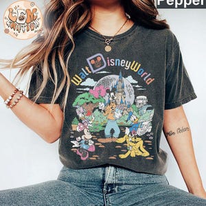 May include: A black t-shirt with a vintage-style graphic of Mickey Mouse and friends at Walt Disney World. The text "Walt Disney World" is printed in a colorful arc above the characters.