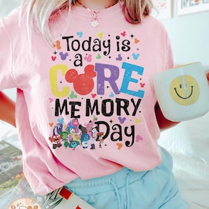 以下が含まれることがあります： ピンクのTシャツに、カラフルなグラフィックがプリントされています。「Today is a CORE MEMORY Day」という文字と、COREの文字の中にミッキーマウスの頭が描かれています。グラフィックには、映画「インサイド・ヘッド」のキャラクターも描かれています。