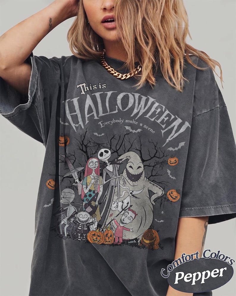 Pu&ograve; includere: T-shirt grigio scuro con grafica di "Nightmare Before Christmas". Il design include personaggi come Jack Skellington, Sally e Oogie Boogie, con la scritta "This is Halloween". La maglietta &egrave; Comfort Colors Pepper.