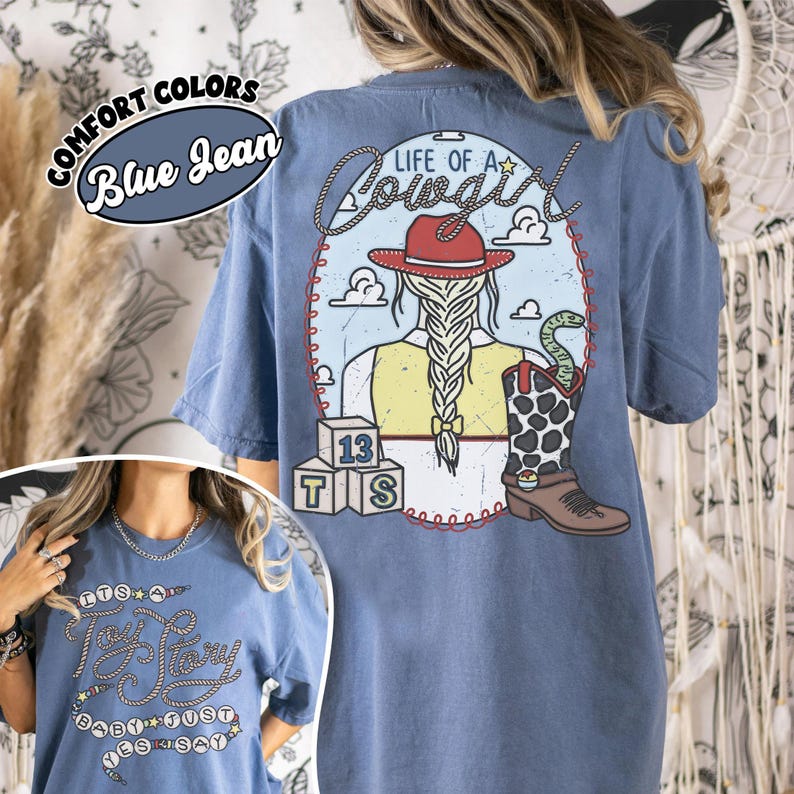 May include: A blue jean colored t-shirt featuring a back graphic of a cowgirl with a braided ponytail, a red hat, and a cow-print boot with a snake. The text reads Life of a Cowgirl, 13, T, S. The front graphic features the text It's a Toy Story baby just yes say.