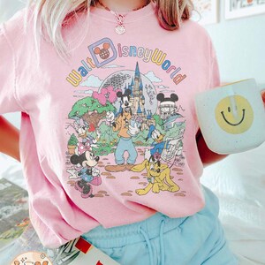 May include: A pink t-shirt with a vintage-style graphic of Mickey Mouse and friends at Walt Disney World. The graphic features the text "Walt Disney World" in a rainbow font.