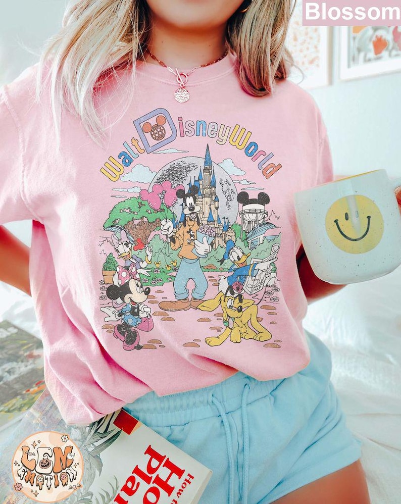 May include: A pink t-shirt with a vintage-style graphic of Mickey Mouse and friends at Walt Disney World. The graphic features the text "Walt Disney World" in a rainbow font.