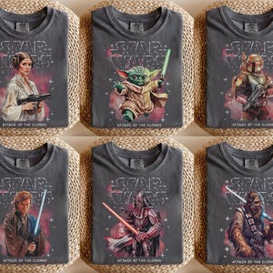 K&ouml;nnte beinhalten: Sechs graue T-Shirts mit Star Wars-Charakteren. Jedes Shirt hat das Star Wars-Logo und den Text "ATTACK OF THE CLONES". Zu den Charakteren geh&ouml;ren Prinzessin Leia, Yoda, Boba Fett, Anakin Skywalker, Darth Vader und Chewbacca.