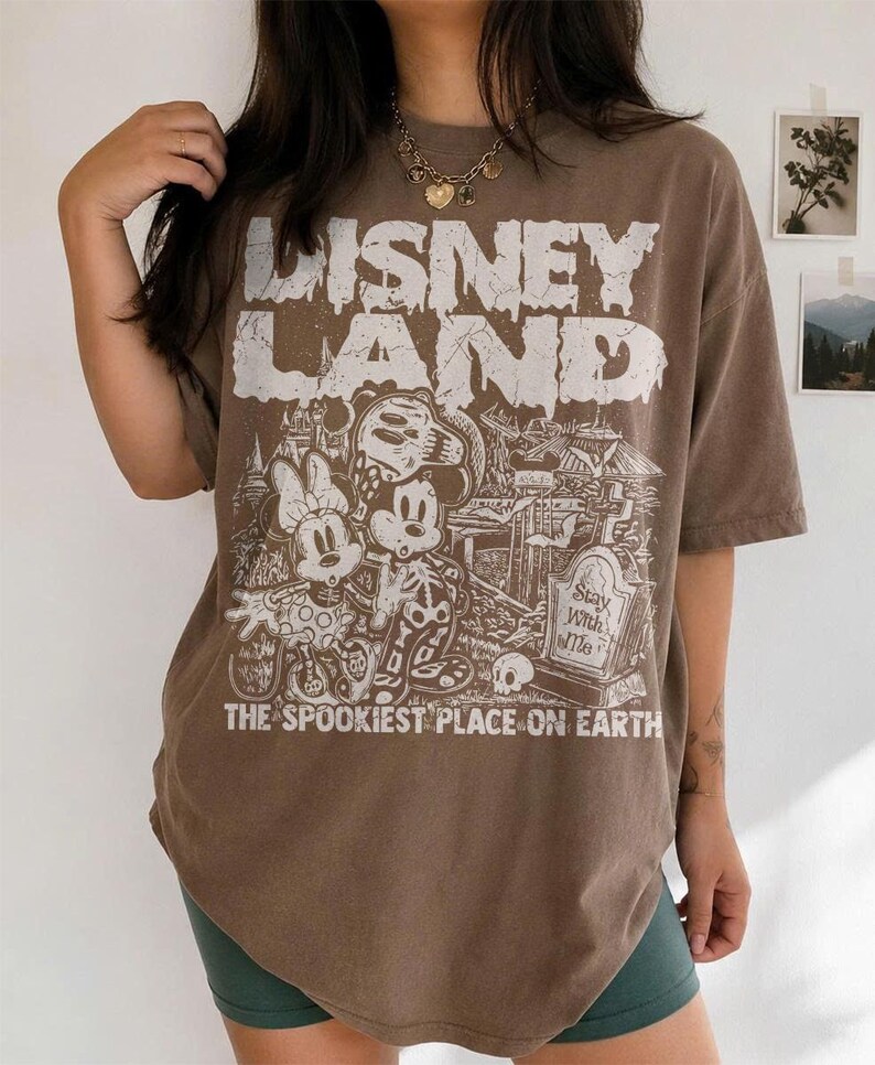 May include: Brown t-shirt with a distressed "Disney Land" graphic. The graphic features Mickey and Minnie Mouse in skeleton costumes, a graveyard scene, and the text "The Spookiest Place on Earth."