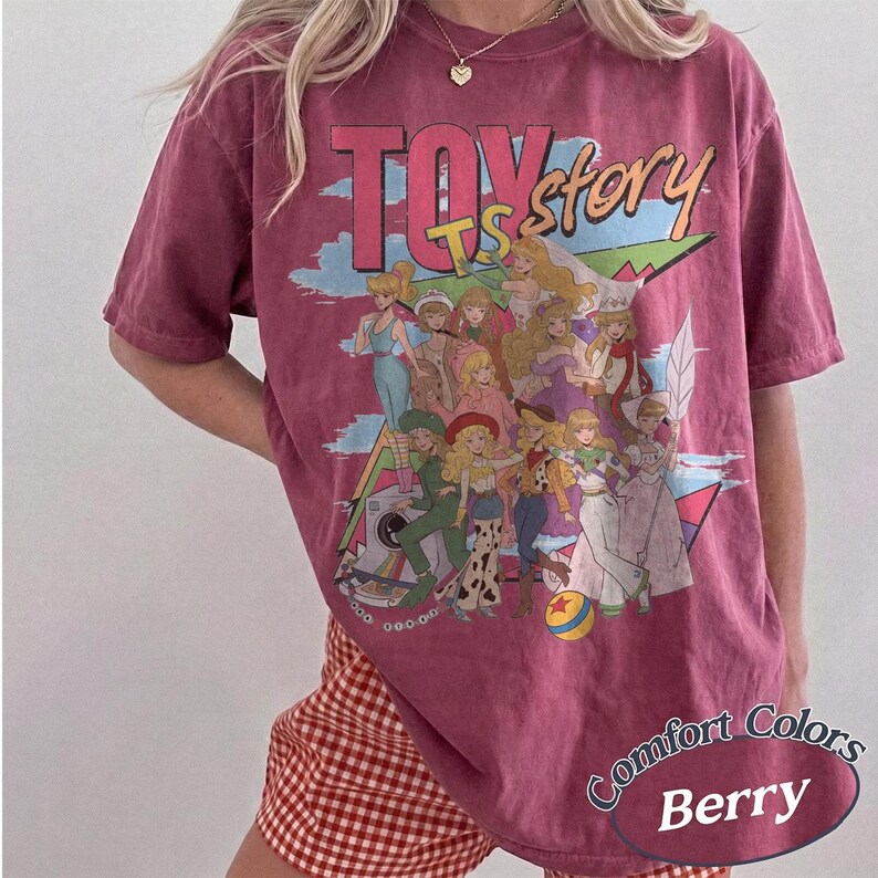 Peut inclure: Un t-shirt &agrave; manches courtes de couleur baie avec une impression graphique portant le texte "TOY story" en grandes lettres. Le motif montre un groupe de personnages f&eacute;minins illustr&eacute;s aux cheveux blonds dans diverses tenues et une petite balle.