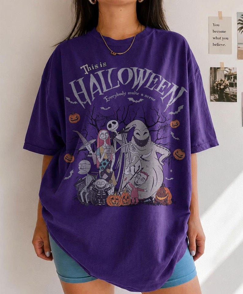 Pu&ograve; includere: Una maglietta viola con una grafica del film "Nightmare Before Christmas". Il design include Jack Skeletron, Sally e altri personaggi, con la scritta "This is Halloween" e "Everybody make a scene."