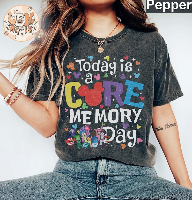 以下が含まれることがあります： レインボーカラーで「Today is a CORE MEMORY Day」と書かれたダークグレーのTシャツ。テキストは小さなミッキーマウスの耳で囲まれています。Tシャツには、映画「インサイド・ヘッド」のアニメキャラクターも描かれています。
