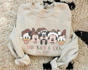 May include: A light gray sweatshirt with a Christmas-themed design featuring Mickey Mouse, Minnie Mouse, Donald Duck, and Goofy wearing Santa hats. The text "MICKEY & CO. Est. 1928" is printed below the characters.