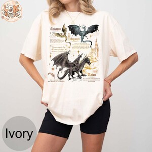 May include: A white t-shirt with a graphic of three dragons and their names: Andarna, Sgaerel, and Tairen. The dragons are drawn in a vintage style with gold accents.