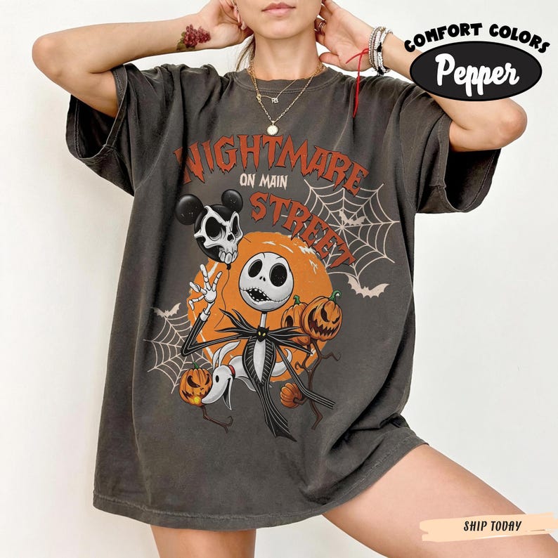 Pu&ograve; includere: Una t-shirt a maniche corte grigio antracite con una stampa grafica recante il testo Nightmare on Main Street. Il design include un personaggio scheletro, un cane fantasma, zucche, ragnatele e pipistrelli nei colori arancione, bianco e nero.