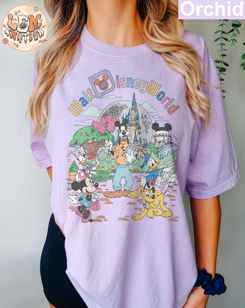 May include: A purple t-shirt with a vintage-style graphic of Mickey Mouse and friends at Walt Disney World. The text "Walt Disney World" is written in a colorful arc around the characters.