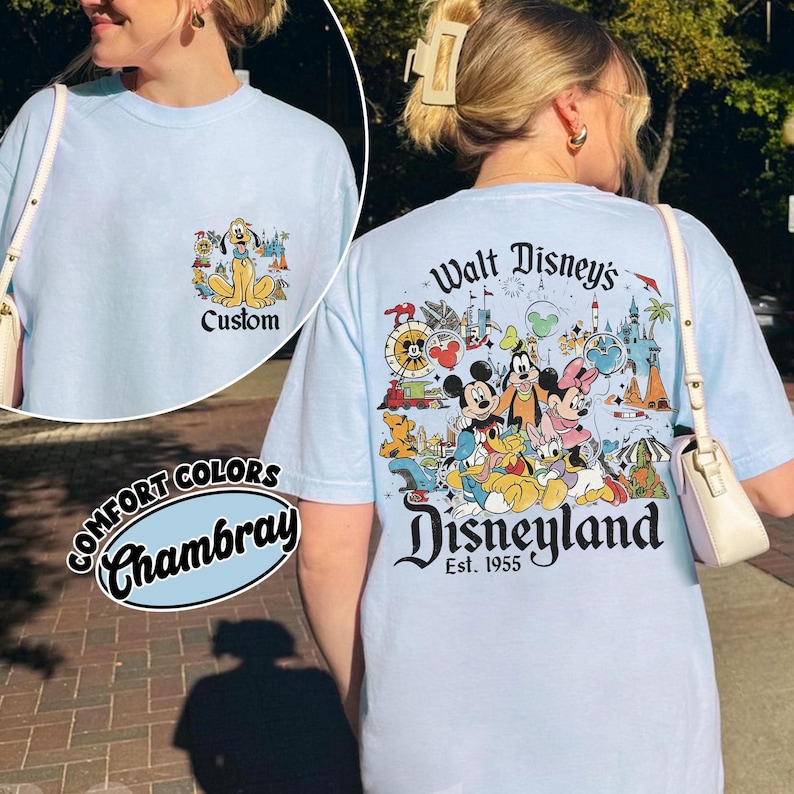Puede incluir: Camiseta azul claro con un gr&aacute;fico de Disneyland en la espalda y un gr&aacute;fico m&aacute;s peque&ntilde;o de Pluto en la parte delantera. El gr&aacute;fico de la espalda presenta a Mickey Mouse, Minnie Mouse, Donald Duck y otros personajes de Disney. La camiseta tiene el texto "Custom" en la parte delantera.