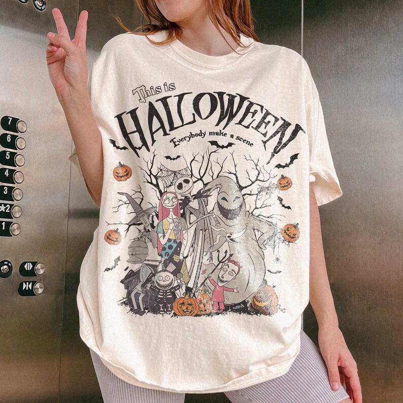 Pu&ograve; includere: T-shirt color crema con grafica da "Nightmare Before Christmas". Il design include Jack Skellington, Sally, Oogie Boogie e altri personaggi, con la scritta "This is Halloween" e "Everybody make a scene."