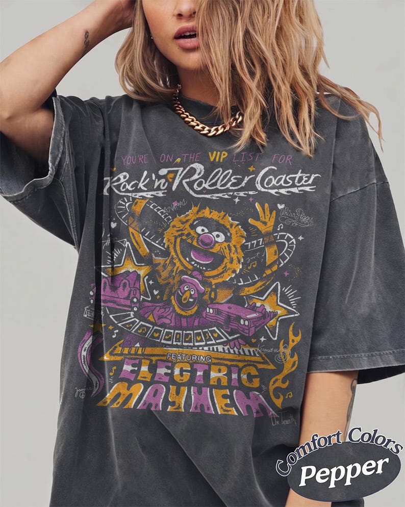 Puede incluir: Camiseta gris oscuro con un gr&aacute;fico que presenta un personaje de los Muppets y el texto "Rock'n Roller Coaster" y "Electric Mayhem". La camiseta est&aacute; etiquetada como "Comfort Colors Pepper".