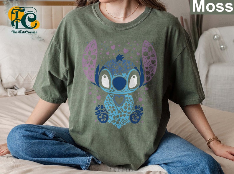 May include: A green t-shirt with a blue and purple floral Stitch design. The design features Stitch's signature big eyes and a floral pattern.